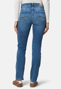Sötétkék farmernadrág, slim fit szabással, öt zsebes kialakítással és látható varrással a hátsó zsebeknél. Kopott hatások az alján.