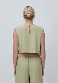 Korte mouwen, cropped top in lichtgroene stof met een kleine sleutelgatopening op de rug. Gecombineerd met bijpassende lichtgroene broek.