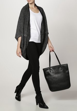 Cardigan en style kimono à motifs noirs, t-shirt blanc, jeans skinny noirs et sac fourre-tout en cuir noir, associés à des bottines à talons noires.