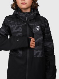 Junge Person, die eine schwarze und graue Jacke mit Camouflage-Muster und Kapuze trägt, mit einer Hand teilweise im linken Ärmel, wobei der Daumen hindurchschaut.