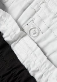 Tissu à taille élastique noir et blanc, présentant une texture lisse et un détail de bouton central. Gros plan sur les coutures et les couches de tissu.