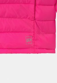 Pohodlná růžová bunda s prošívanou texturou, s logem "GAP" v šedé barvě umístěným v levém dolním rohu. Hladký, lesklý materiál.