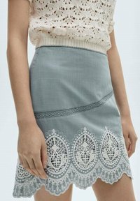 Jupe bleu clair en tissu texturé, ornée d'un délicat galon en dentelle blanche à motifs floraux à l'ourlet et d'une taille lisse.