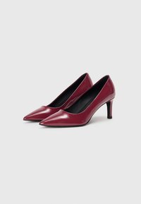 Bordeaux-lakkaiset korkokengät, joissa on terävä nenä ja hoikka stiletto-korko. Sileä pinta kiiltävällä viimeistelyllä.
