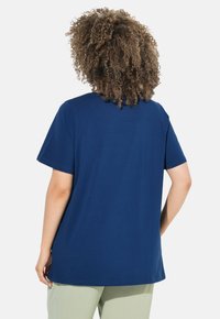 Námořnická modrá bavlněná trička s krátkým rukávem, kulatým výstřihem, volným střihem a rovním zakončením, kombinovaná se světle zelenými kalhotami.