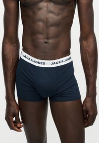 Torso masculin portant un boxer Jack & Jones bleu marine avec une ceinture blanche affichant le nom de la marque en lettres noires.