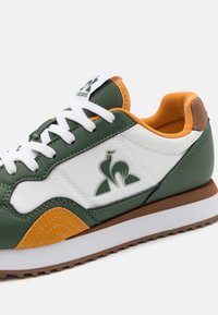 Baskets multicolores avec cuir vert et accents blancs et orange, semelle en caoutchouc et détail de logo sur le côté.