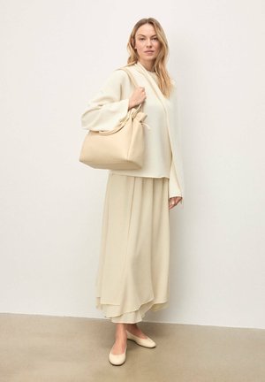 Pull crème à manches larges associé à une jupe fluide assortie. Un sac à main beige doux avec un nœud en accent complète la tenue, accompagné de chaussures légères.