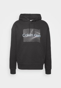 Felpa nera con cappuccio in misto cotone, con tasca a marsupio frontale e una grafica a linea ondulata bianca con il testo "Calvin Klein".
