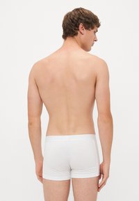Boxers en coton blanc sur un modèle masculin, vus de dos, présentant une coupe ajustée et une texture lisse contre la peau nue.