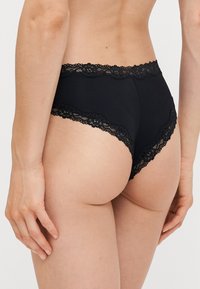 Panties neri a vita alta con pizzi sul girovita e sulle aperture delle gambe, realizzati in un tessuto morbido con una consistenza liscia.