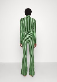 Dwuczęściowy strój w zielono-czarne paski, z górą z wysokim kołnierzem i rozkloszowanymi spodniami, wykonany z dopasowanego, rozciągliwego materiału.