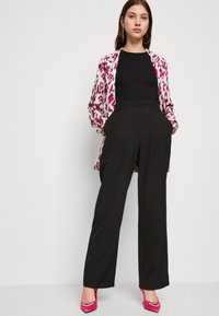 Calças largas pretas, cintura ajustada, combinadas com uma camisa de manga longa em padrão de leopardo rosa e branco, e sapatos de salto rosa com detalhes.