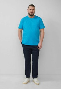 Türkisfarbenes Rundhals-T-Shirt aus Baumwollmischung; marineblaue Cargo-Hosen mit Seitentaschen; weiße Sneakers. Einfaches Design, keine sichtbaren Muster oder Logos.