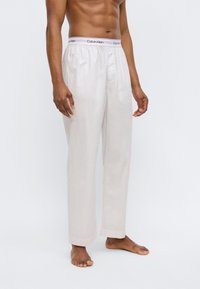 Παντελόνι πυτζάμας από βαμβάκι ανοιχτού χρώματος με ελαστική μέση που φέρει το λογότυπο Calvin Klein, σε ίσια γραμμή και χωρίς ορατά σχέδια ή διακοσμητικά στοιχεία.