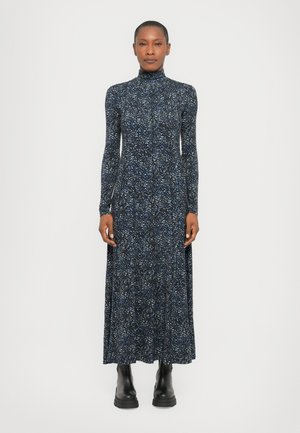 Long-sleeve, high-neck dress in dark navy with a multicolored splatter pattern; made of soft fabric. Worn with black ankle boots.