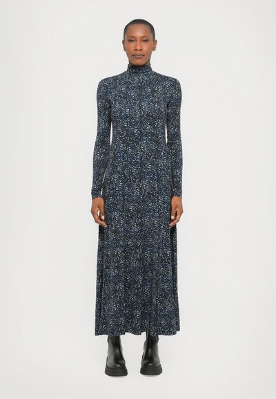 Robe à manches longues et col montant en bleu marine foncé avec un motif éclaboussé multicolore ; confectionnée en tissu doux. Portée avec des bottines noires.
