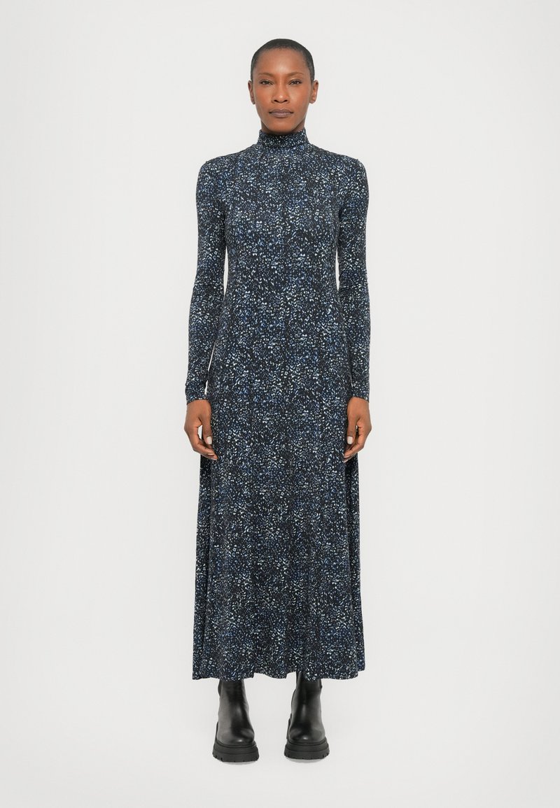 Long-sleeve, high-neck dress in dark navy with a multicolored splatter pattern; made of soft fabric. Worn with black ankle boots.