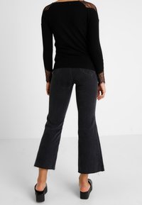 Pull noir ajusté avec des accents en dentelle sur les épaules, associé à un jean gris foncé évasé et des sandales compensées noires.