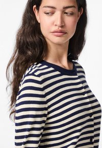 Ριγέ ζακέτα με οριζόντιες ρίγες σε ναυτικό μπλε και κρεμ, με στρογγυλεμένο λαιμόκοψη και κούμπωμα με κουμπιά μπροστά.