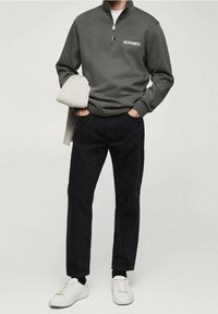 Sweat-shirt gris à fermeture éclair avec le texte "HUMANITY", associé à un pantalon noir et des baskets blanches, présentant un design décontracté et moderne.