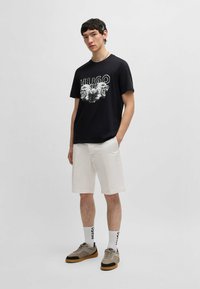 T-shirt noire avec un design graphique représentant trois tigres, associée à un short blanc et des baskets grises avec des accents noirs.