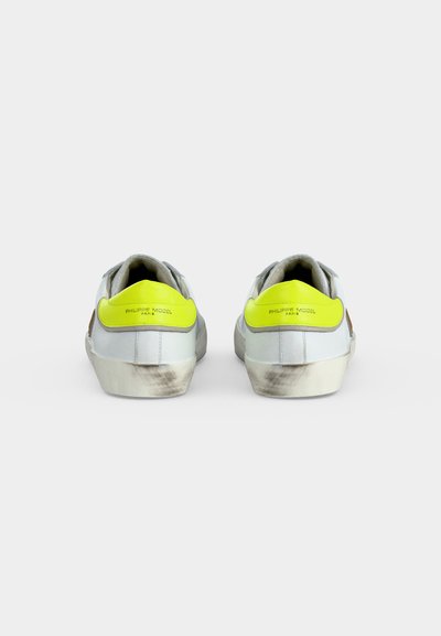 Paire de baskets blanches vue de dos, talons jaunes avec le texte "Philippe Model Paris", semelles légèrement sales.