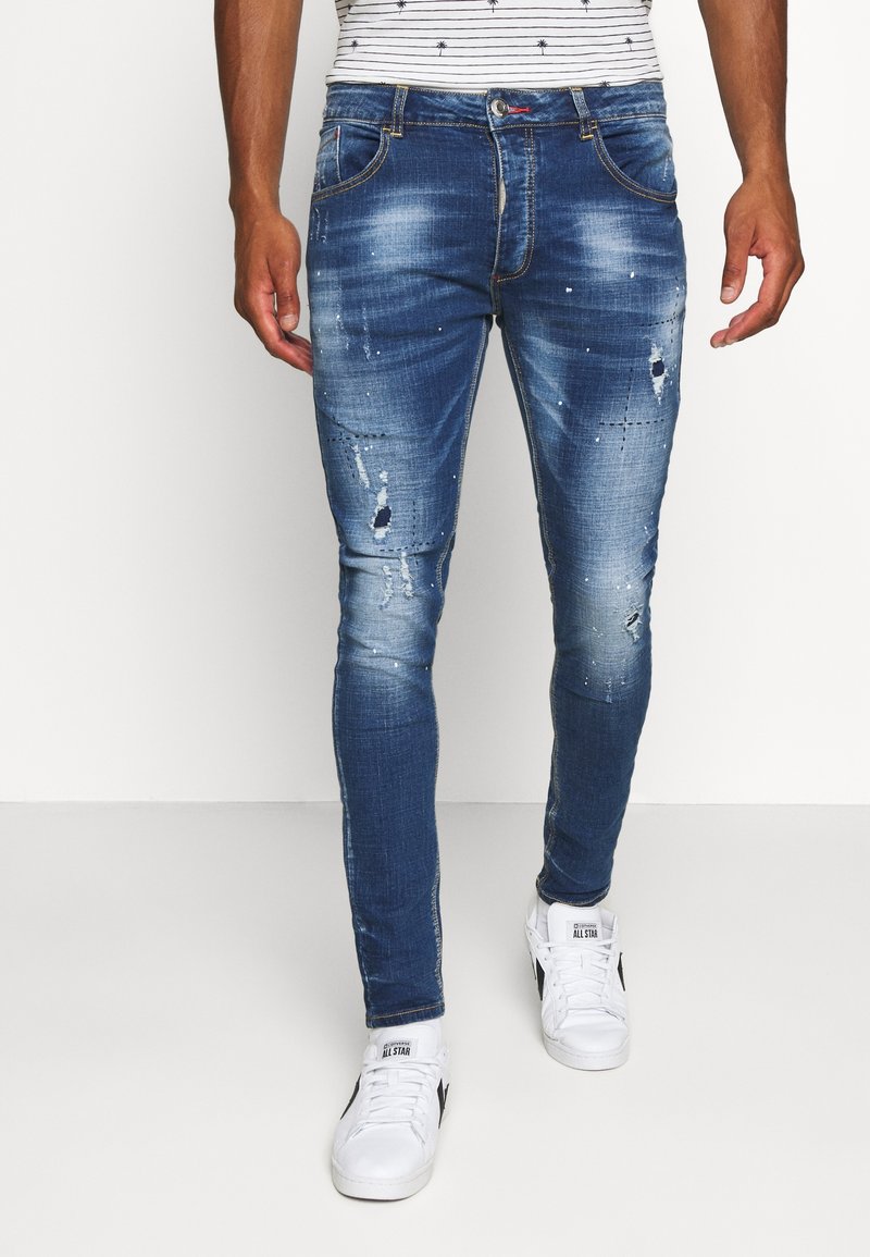 Niebieskie jeansy z denimu o wąskim kroju, z przecieranymi detalami, wyblakłym efektem i zwężanymi nogawkami. Zestawione z białymi trampkami.