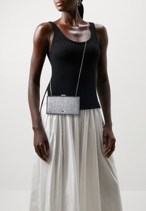 Stříbrná obdélníková kabelka s texturovaným povrchem, řetízkem a zavíráním na klips, v kombinaci s černým topem bez rukávů a bílou plisovanou sukní.