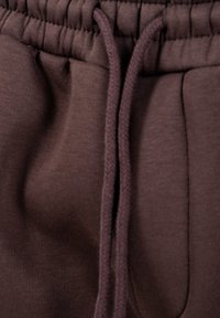 Brune sweatpants i stof med elastisk taljebånd og matchende snore, centreret i billedet.