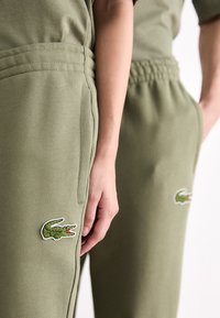 Olijfgroene sweatpants met zijzakken, geribbelde tailleband en geborduurd krokodillologo op het onderbeen. Zachte katoenmix.