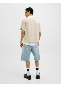 Beige kortærmet skjorte med krave, parret med lyseblå denim shorts. Sorte sko og hvide strømper med sorte striber fuldender looket.