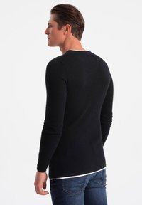 Black long-sleeve shirt made of textured fabric, featuring a crew neckline and minimal stitching details, paired with blue jeans.