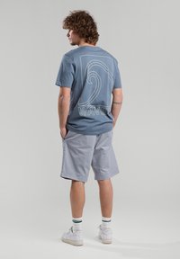 Light blue cotton t-shirt with a wave graphic design and "WAVES" text. Paired with gray shorts and white sneakers with green-striped socks.