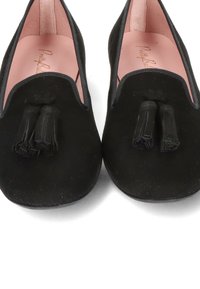 Chaussures plates noires en tissu doux, avec un bout arrondi et deux pompons en tissu à l'avant. L'intérieur est rose clair.