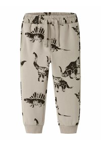 Pantalones de chándal beige para niños con cintura elástica, cordón, tobillos acampanados y estampados de dinosaurios negros que incluyen estegosaurios y triceratops.