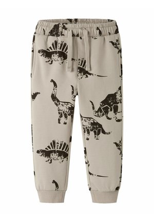 Jogging en beige pour enfants avec taille élastique, cordon de serrage, chevilles élastiquées et imprimés de dinosaures noirs incluant le Stégosaure et le Tricératops.