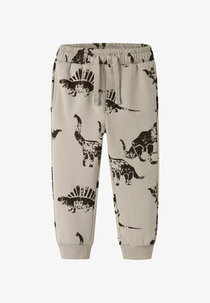 Beige kinder sweatpants met elastische tailleband, trekkoord, manchetten bij de enkels en zwarte dinosaurustafels, waaronder Stegosaurus en Triceratops.