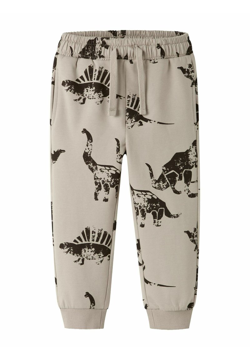 Pantalones de chándal beige para niños con cintura elástica, cordón, tobillos acampanados y estampados de dinosaurios negros que incluyen estegosaurios y triceratops.