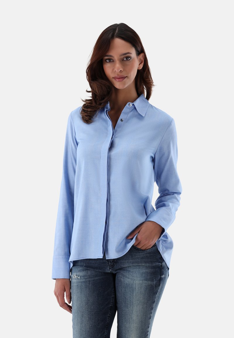 Hellblaues Hemd mit langen Ärmeln, Kragen, einer einzelnen Brusttasche und Schlitzdetails an den Seiten, kombiniert mit dunklen Jeans.