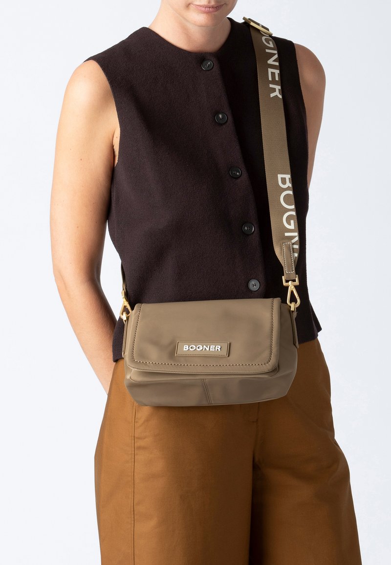 Hnědá crossbody taška obdélníkového tvaru, hladkého povrchu a zlatým kováním. Má logo a nastavitelný popruh s textem.