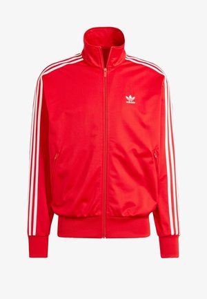 Veste zippée rouge Adidas avec col haut, rayures blanches sur les épaules, deux poches latérales et un petit logo blanc sur la poitrine gauche. Texture lisse.
