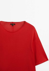 Haut rouge à manches courtes avec un col rond, fabriqué en tissu léger. Présente un design simple et une étiquette de la marque visible à l'intérieur du cou.