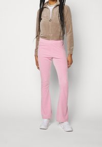 Benvit sammet zip-jacka, matchad med rosa utställda byxor. Modellen bär vita sneakers. Nyckelfunktioner inkluderar slät textur och figurnära design.