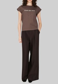 T-shirt en coton marron avec des manches courtes roulées et le texte "Pont des Arts". Assorti à un pantalon large noir, offrant une coupe décontractée.