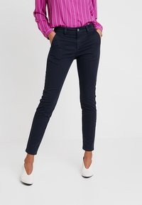 Granatowe spodnie o dopasowanym kroju, wykonane z lekkiego materiału, z zapięciem na guzik i dwoma przednimi kieszeniami. Gładka faktura, nowoczesny design.