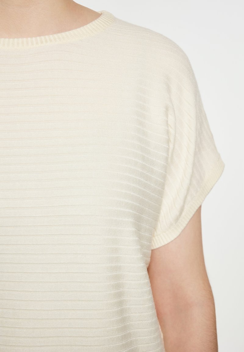 Top color crema con una texture a coste, scollatura rotonda e maniche corte, con sottili righe orizzontali per un dettaglio visivo.