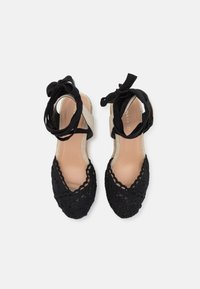 Black crochet espadrille shoes with a woven texture, open toes, ankle ties, and a contrasting beige footbed.