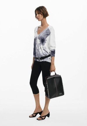 Sac fourre-tout noir avec des coutures contrastées, doté d'un design structuré et de poignées supérieures. Porté avec un haut graphique à manches longues blanc et gris et un legging.
