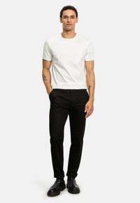 Weißes T-Shirt mit kurzen Ärmeln, kombiniert mit schwarzen Hosen. Das Modell trägt schwarze Knöchelstiefel. Einfaches Design mit einer taillierten Silhouette.